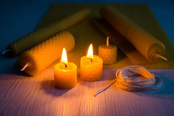 Natural rolled beeswax candles from pressed beeswax honeycomb sheet at home indoors. Hobby concept. Two candles lit and burning in the dark.
