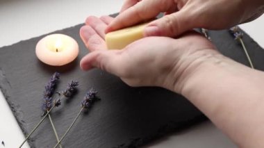 Handmade beeswax and shea butter solid moisturizing hand cream. Heart shape cream bar made of all natural ingredients. Background with dried lavender flowers and candle burning.