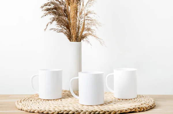 stock image Three white empty mugs mock up. Multiple cups on wood table with white vase with reed and wood lantern for decoration. Lot of empty copy space.