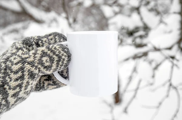 stock image Traditional pattern mitten holding white blank coffee mug mock up template. Cozy seasonal products advertisement background. Single cup on snowy Scandinavian winter nature background. Room for text.