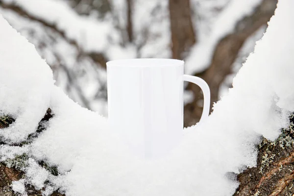 White blank coffee mug mock up template. Cozy seasonal products advertisement background. Single cup on snowy Scandinavian winter nature background. Room for text.
