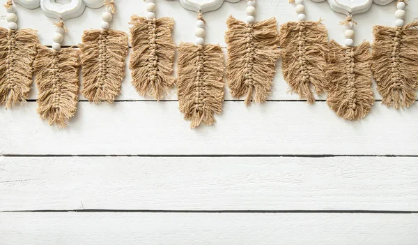 stock image Light brown leaf or feather shape macrame hanging against white wood board background in home room. Lot of copy space, boho background.