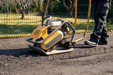 Ev sahibinin yakın görüntüsünü kapatın. Baharda bahçedeki bahçeye geri dönüşümlü asfalt çiplerle otopark yapmak için plaka sıkıştırıcı kullanın..