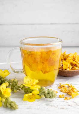 Verbascum thapsus 'tan yapılmış bitkisel tıbbi çay içeceği, büyük mullein, büyük mullein ya da yaygın mullein. Sarı kurutulmuş çiçek yaprakları. Beyaz arka planda çay fincanı ve kasede kurumuş yapraklar..