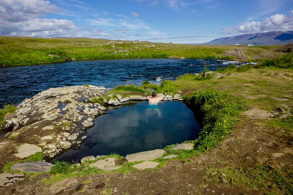 自然地熱温水プール 夏にアイスランドの温泉でリラックスして入浴する人 背景に緑の丘陵と青空 温泉はフォスラウグ鍋と呼ばれています — ストック写真