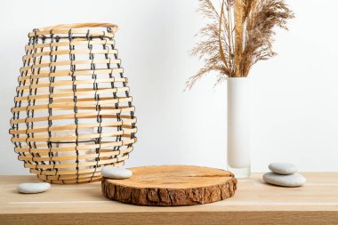 Minimum doğal ahşap ev dekorasyonu, çam ağacından yapılmış disk kaidesi, vazoda kuru kamış ve mum yanan yuvarlak ahşap fener, arka planda beyaz duvar. Ev içi arkaplan.