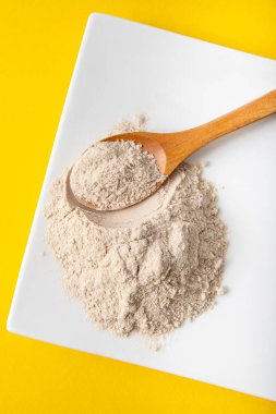 Beyaz tabakta psilyum kabuğu un tozu ve evde ahşap kaşık, sarı arka plan. Psyllium un konseptinin sağlık faydaları.