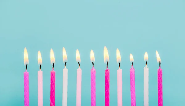 11 pink and white color birthday candles burning in a row isolated on blue. Happy Birthday card design concept.  Bottom lower border edge a lot of copy space.