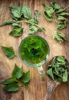 Isırgan otu, ısırgan otu ya da cam bardaktaki ısırgan otu yaprakları olarak bilinen kuru Urtica dioica bitkisinden yapılmış bitki çayının üstünde. Ev mutfağında ahşap arka plan.