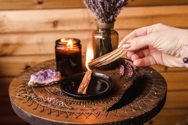 Kadın el ele tutuşuyor ve Palo Santo tahta çubuklarını kullanıyor. Eski negatif enerjiden ev temizleme seansı için duman çıkıyor. Yağlı aromalı kutsal ahşap sopalar elinde yanıyor..