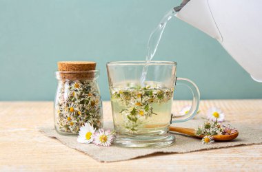 Elektrikli çaydanlıktan bitkisel çay bardağına kaynar su dökülüyor. Kurutulmuş bitkisel bitki. Yaygın bitki Daisy. Bellis Perennis olarak da bilinir. Kuru çiçekler cam kavanozda ve bitkisel çaylar da bardakta..