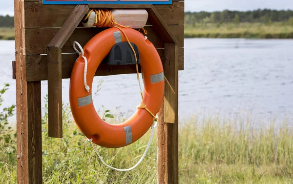 Orange color round self help lifebuoy by small local swimming spot by lake, no public lifeguard. Beautiful summer lake landscape with copy space.