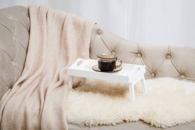 Beyaz ahşap kahvaltı tepsisi. Bacakları kanepenin üzerinde. Bir fincan sıcak kahve, mumlar yanıyor. Yumuşak yün battaniyeli Hygge düzenlemesi.