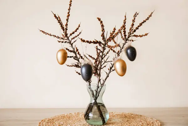 Tree branches in vase with colored Easter eggs hanging on string. Nice warm beige earthly tones. Minimal home Easter decoration.