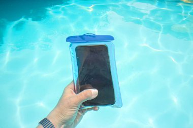 Güzel mavi havuzda, tropikal bir yerde el ele tutuşan akıllı telefonlar. Etkilenen kadın kavramı, su geçirmez bir çantanın içindeki akıllı telefonla video ve fotoğraf çeker.. 