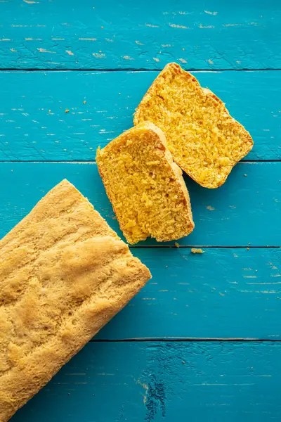 stock image Beautiful homemade yellow sliced cornbread loaf on blue wood board background. Above view, rustic look.