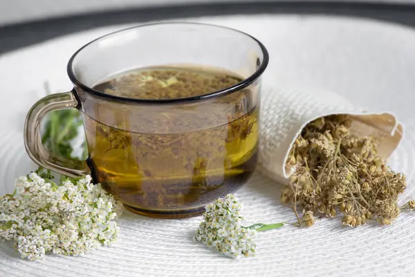 stock image Still life of Achillea millefolium, yarrow or common yarrow herbal medicinal tea in glass with dry tea powder and fresh blossoms on white minimal set background.