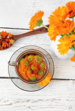 Calendula officinalis the pot marigold, ruddles, common marigold ya da Scotch marigold, çiçek çayını berrak bardakta ekin, tıbbi tedavi kavramı. Beyaz tahta arka plan. Kurutulmuş çay..