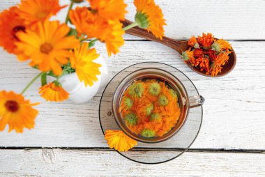Calendula officinalis the pot marigold, ruddles, common marigold ya da Scotch marigold, çiçek çayını berrak bardakta ekin, tıbbi tedavi kavramı. Beyaz tahta arka plan. Kurutulmuş çay..