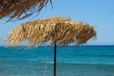 Doğal malzeme kuru kamış yaprağı güneş şemsiyesine karşı durgun turkuaz su, mavi gökyüzü. Seyahat ve tatil geçmişi kavramı.