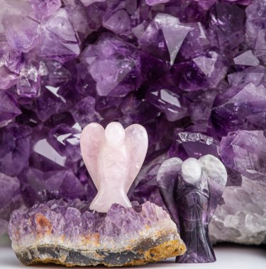 Gül kuvars ve ametist melek şekilli heykelciklere karşı kapalı alanda ametist jeot kristali, stüdyo çekimi. Ruhani ev dekorasyonu kavramı. 