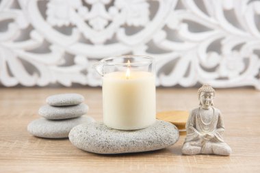 Ev yapımı masaj yağı mumu, cam bardakta, ağız ile. Bohem tarzı arka plan, oturan Buda heykeli, kompozisyonu rahatlatmak için zen taşları dizilmiş.