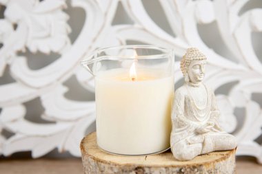 Ev yapımı masaj yağı mumu, cam bardaktan dökülmüş. Bohem tarzı arkaplan, dekorasyon için Buda heykelciği oturuyor.