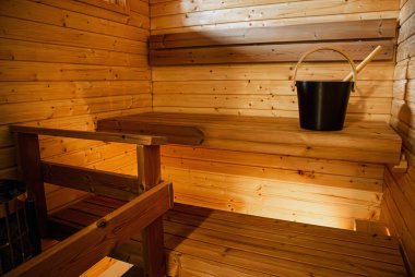 Küçük iki kişilik Finlandiya saunası. Siyah renkli sauna kovası ve tahta bankta sauna kepçesi..
