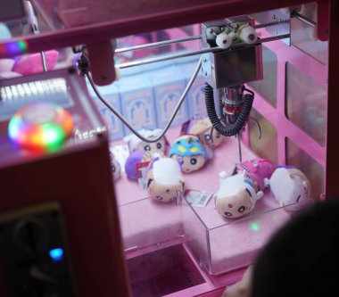 Çocuk atari salonunda pençe oyunu oynuyor. Oyuncak bebekleri pençelerinden tutuyor..