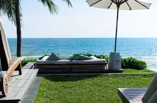 Sahile, denize, plaj şemsiyelerine, hindistan cevizi ağaçlarına ve yeşil çimenlere bakan koltuklar. mavi gökyüzü ve çimen