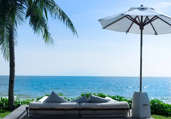 Sahile, denize, sahil şemsiyelerine, hindistan cevizi ağaçlarına ve yeşil çimenlere bakan kanepe seti. mavi gökyüzü