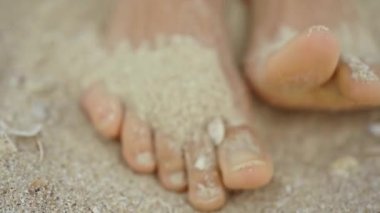 POV, sıcak yaz güneşli bir günde kumsalda deniz kabukları ile beyaz kum üzerinde kadın ayak ve ayak parmaklarını ilk kez görüyor. Seyahatte rahatlama ve sağIık kavramı