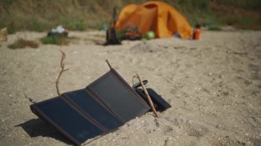Güneş paneli kumsalda yaz günü kamp alanında kumlara elektrik yüklüyor. arkaplanda turuncu çadır