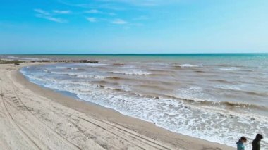 Ukrayna 'daki Azov deniz dalgaları boyunca yürüyen çiftin hava görüntüsü. Sarı beyaz kum ve dalgalı deniz yaz deniz manzarası. Su ve sahil dokusu. Doğal deniz manzarası. 4K