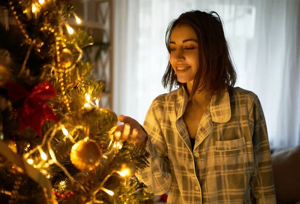 圣诞快乐 新年快乐 身着舒适的家庭睡衣的年轻女性享受着圣诞树的灯火 为节日庆祝活动感到兴奋 — 图库照片