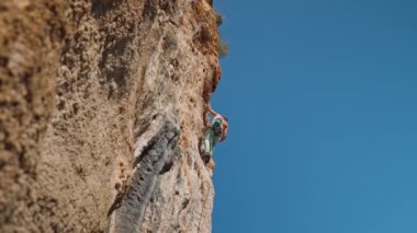 young powerful athletic man rock climber with long hair climbing on cliff. male climbing very hard route making long hard movement. extreme sport, rock climbing outdoors, training moments