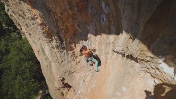 長い髪を持つ若い強力なアスレチックマンロッククライマーは 長い崖の上に登る 男は長いハード移動を作る非常に難しいルートを登る 極端なスポーツや屋外でのロッククライミングトレーニングの瞬間 — ストック動画
