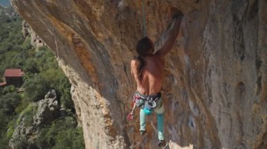 Genç atletik tırmanışçı uzun saçlı kayalıklara tırmanıyor. Erkek çok zor bir yola tırmanıyor sert hareketler yapıyor ve düşüyor. Ekstrem spor, kaya tırmanışı, antrenman anları