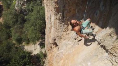 young athletic man rock climber with long hair climbs on the overhanging cliff. male climbing very hard route making hard movement, falling and hanging on rope