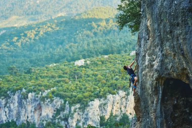 Güzel dağların ve kayaların panoramik görüntüsü, etkin güçlü adam yüksek uçurum duvarına tırmanıyor.