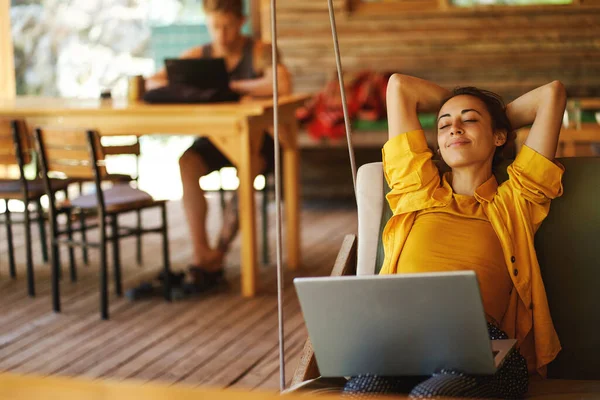 Unbekümmerte Frau Entspannt Mit Ihrem Laptop Auf Der Schaukel Café lizenzfreie Stockfotos