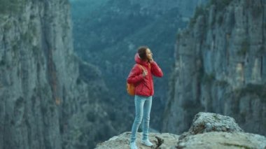 Sırt çantalı, kırmızı ceketli neşeli turist kız uçurumun kenarında yürüyor ve büyük kanyona bakıyor, panoramik manzara. Tazi Kanyonu Türkiye 'de yaygın bir turizm beldesi