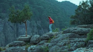 Kırmızı ceketli, sırt çantalı, uçurumun kenarında yürüyen ve panoramik manzaralı bir turist kızın yan görüntüsü. Tazi Kanyonu Türkiye 'de yaygın bir turizm beldesi