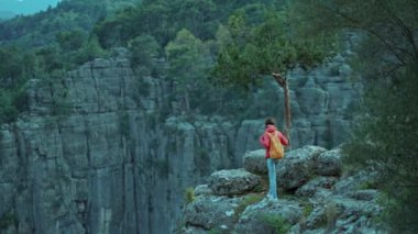 Kırmızı ceketli, sırt çantalı, uçurumun kenarında yürüyen ve panoramik manzaralı bir turist kızın arka görüntüsü. Tazi Kanyonu Türkiye 'de yaygın bir turizm beldesi