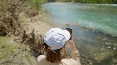 Koprulu Kanyonu 'ndaki dağ nehri kıyısındaki kadın turist panoramik manzaranın fotoğrafını çekiyor. Koprulu Kanyonu Türkiye 'de yaygın bir turizm merkezidir. Kız cep telefonu kamerasıyla fotoğraf çekiyor.