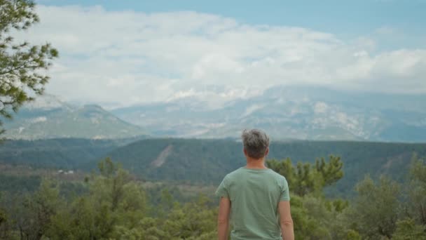 後ろの景色は男が山の背景を歩いて彼の腕を上げるインスピレーションを与えた トルコの自然の美しさと自然の美しさを楽しむ男旅行者 旅行休暇のコンセプト — ストック動画