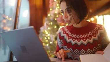 Noel arifesinde Xmass dekore edilmiş kahve dükkanında çalışan ve dizüstü bilgisayar, not defteri, fazla çalışma ve tatil konsepti kullanan stresli bir kadın. Uzak çalışma serbest, proje bitiş tarihi, her şeyi yapmak