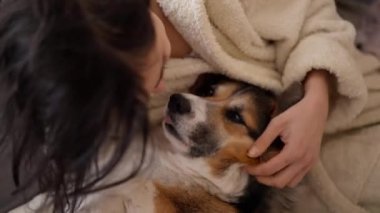 Evcil hayvanını kucaklayan sevecen bir kadın portresi. Şirin Galli Corgi köpeği sahibinin yanında dinleniyor, evde birlikte vakit geçiriyorlar. Köpek ve insanla arkadaşlığı kavra, tatlı anlar, rahatlatıcı, kaygısız.