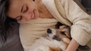 Evcil hayvanını kucaklayan sevecen bir kadın portresi. Şirin Galli Corgi köpeği sahibinin yanında dinleniyor, evde birlikte vakit geçiriyorlar. Köpek ve insanla arkadaşlığı kavra, tatlı anlar, rahatlatıcı, kaygısız.