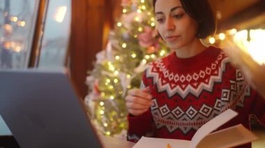 Noel arifesinde Xmass dekore edilmiş kahve dükkanında dizüstü bilgisayar ve defter kullanarak çalışan aşırı çalışan serbest çalışan bir kadın. Uzak çalışma serbest, proje bitiş tarihi, her şeyi yapmak